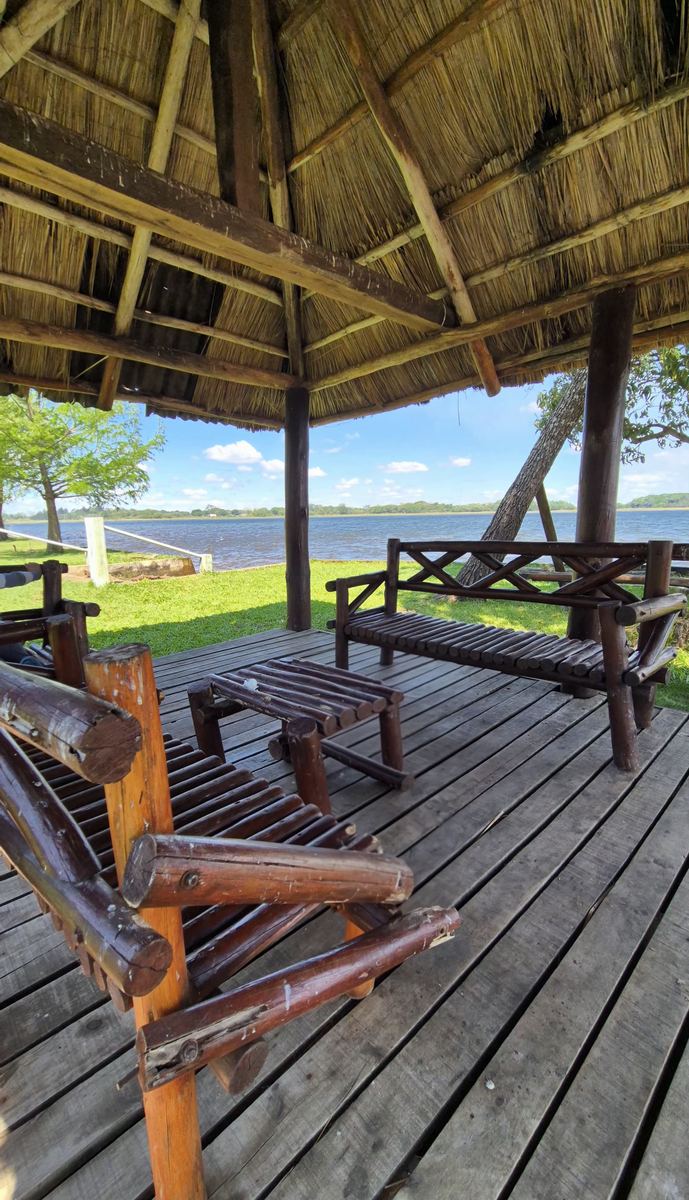 Quincho con techo de paja, deck de madera y bancos mirando a la laguna